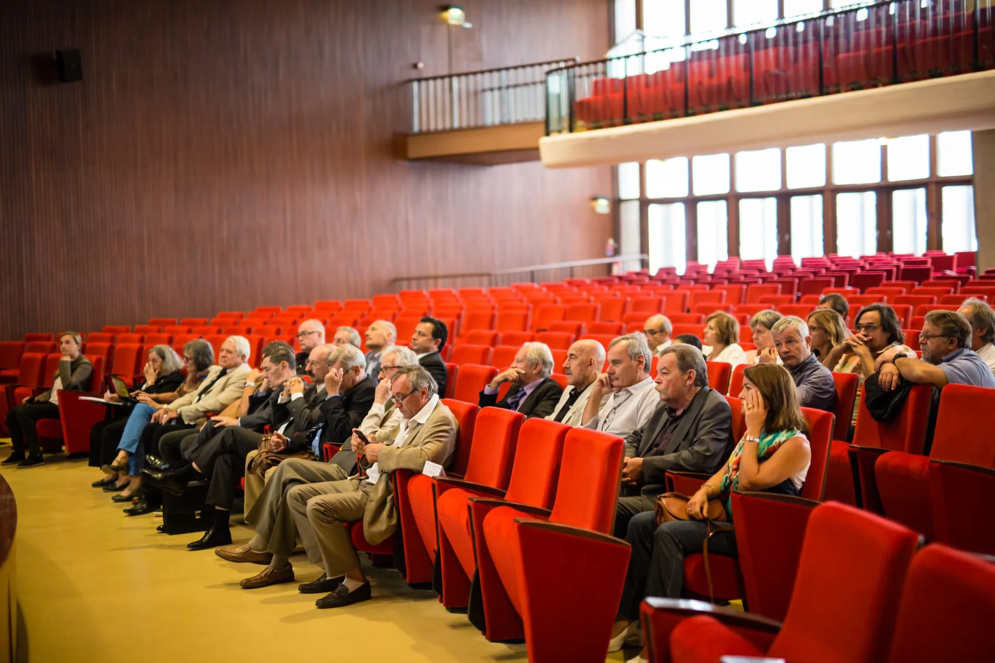 Public assis dans les fauteuils rouges d'un grand amphithéâtre boisé