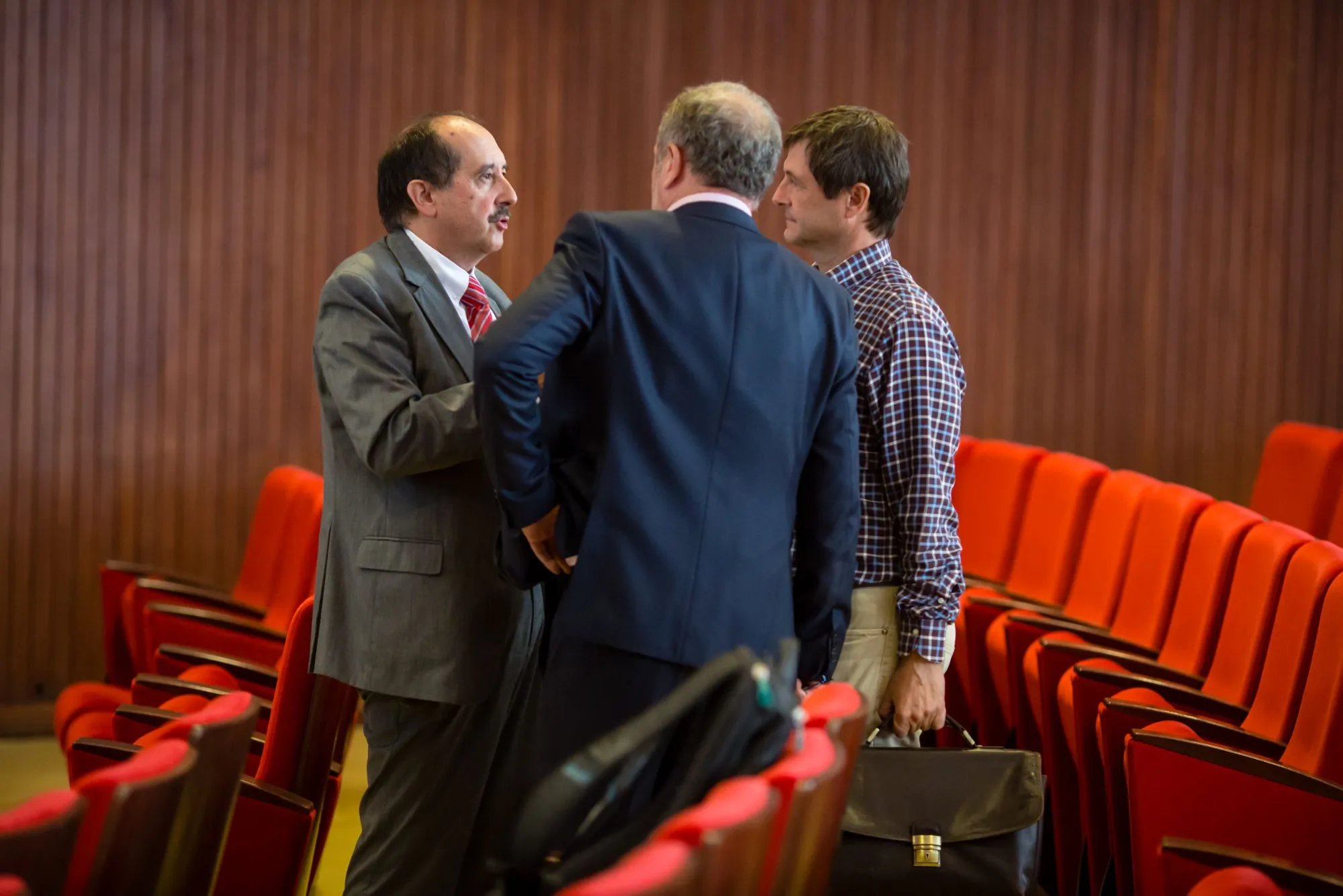 Trois participants en costume discutant entre les rangs de fauteuils rouges