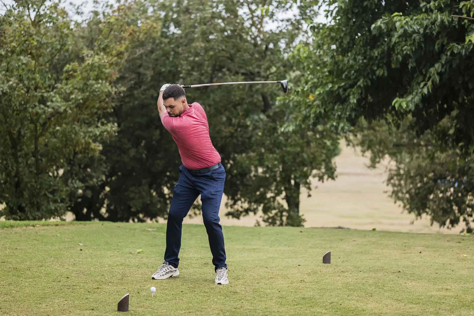 Joueur en polo rouge au sommet de son swing sur l'aire de départ