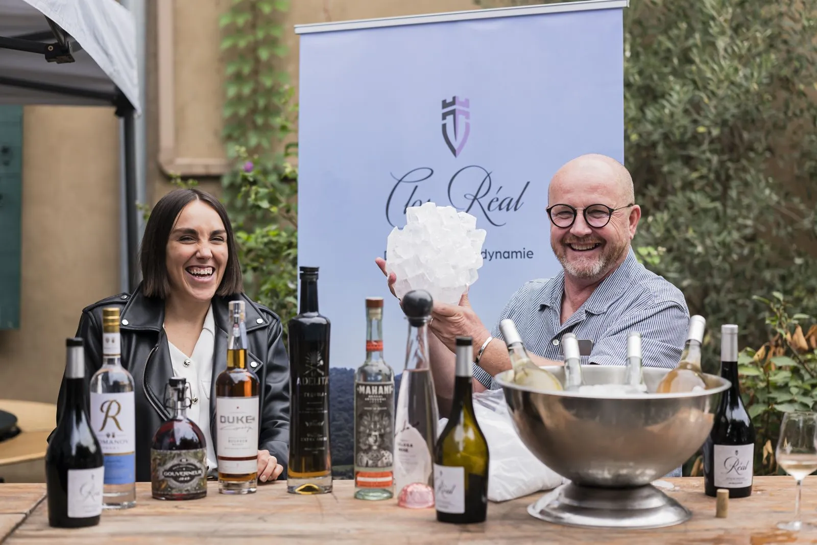Deux exposants riant derrière une table de bouteilles de vins et spiritueux