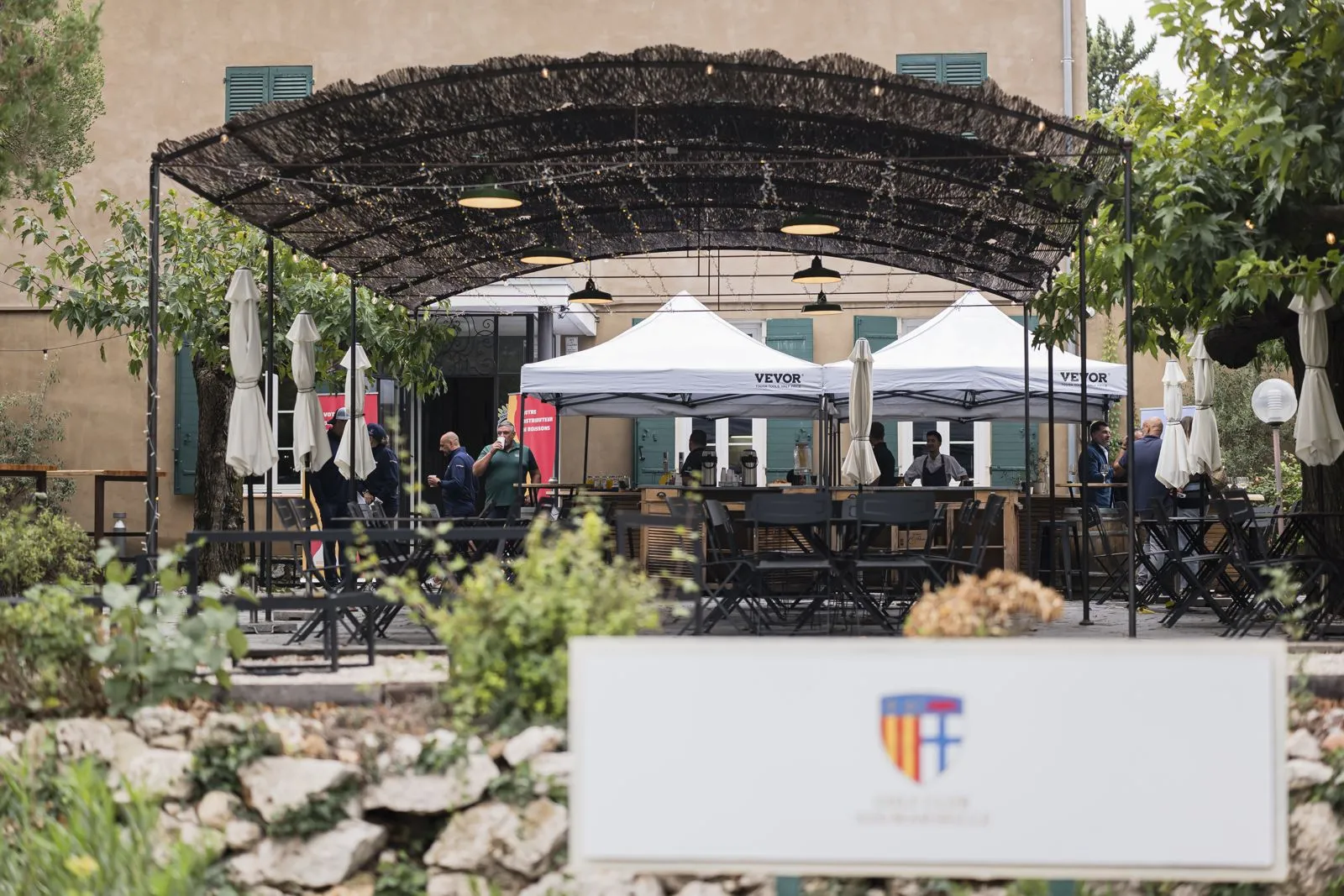 Terrasse du club house sous une pergola, tentes d'accueil et participants
