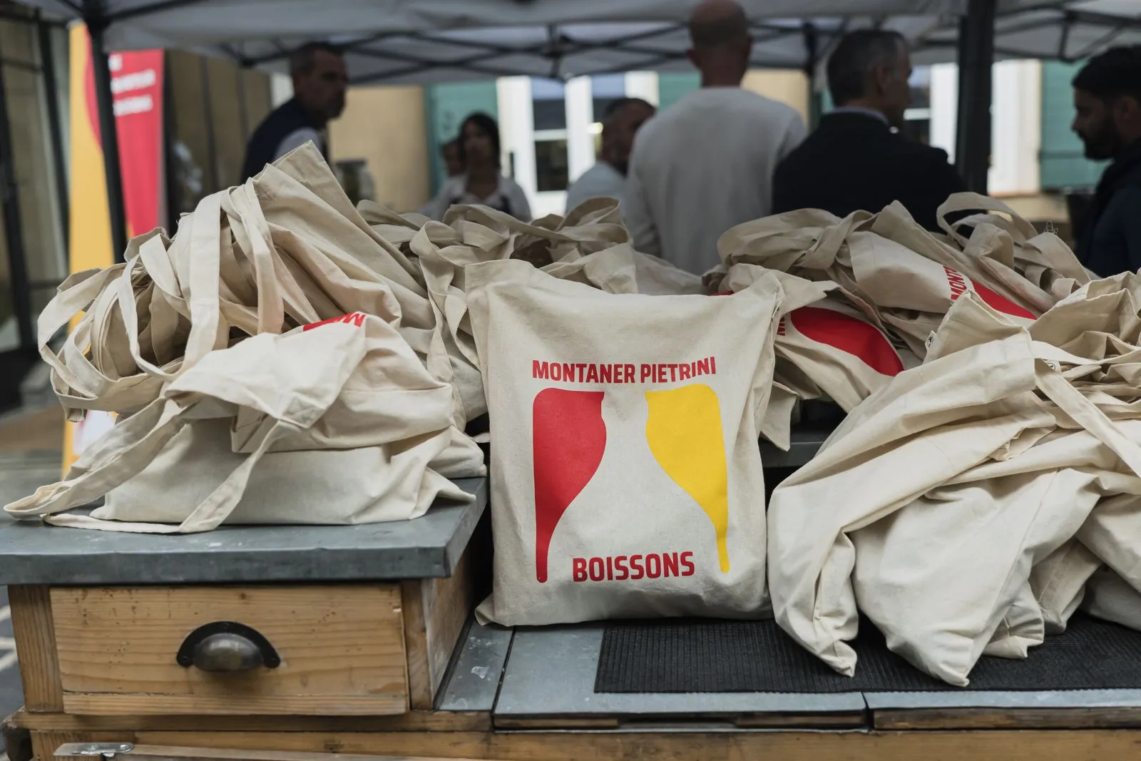 Sacs en toile du partenaire empilés sur une table, invités en arrière-plan
