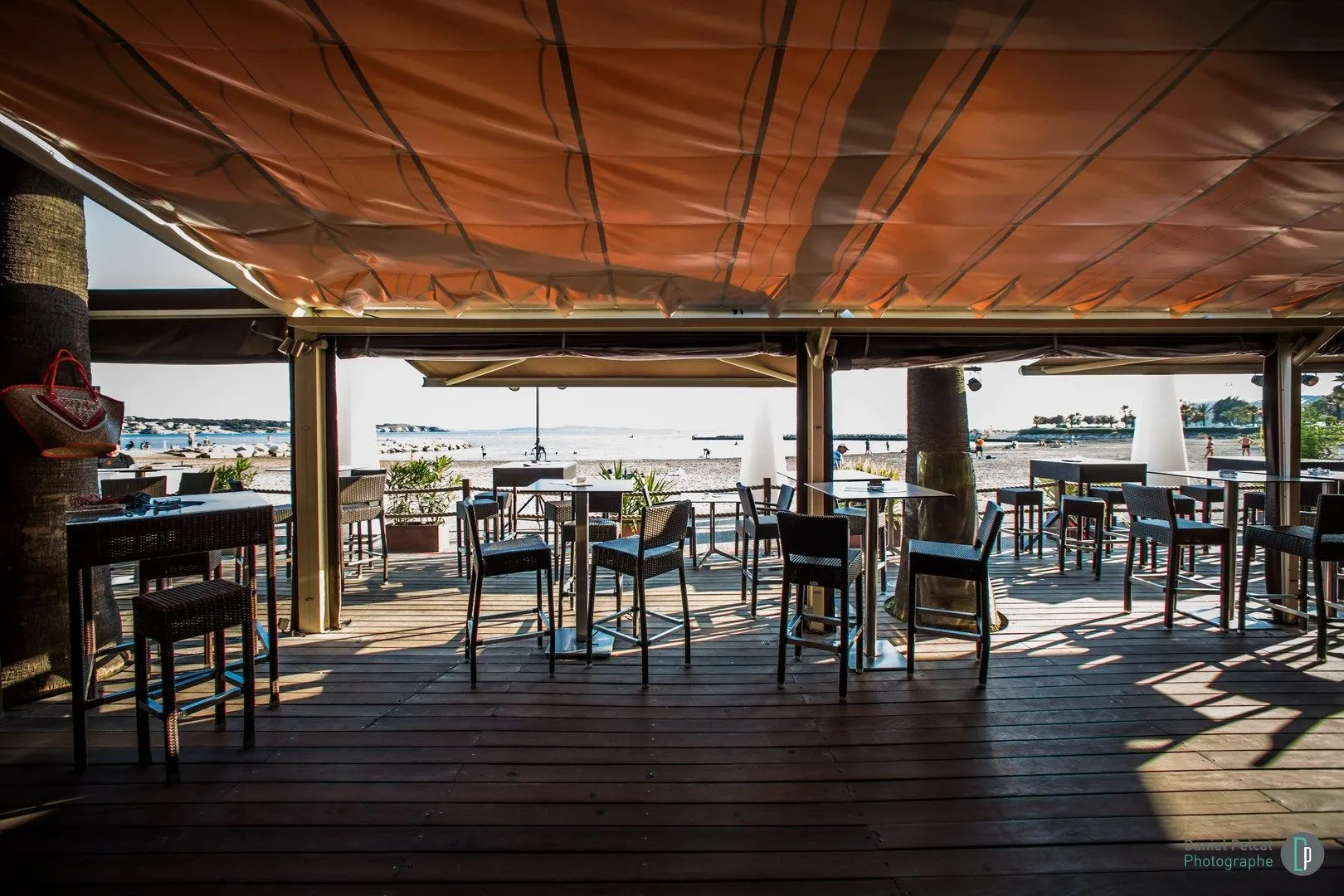 Terrasse abritée par une toile, tables hautes face à la mer