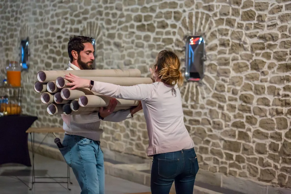 Deux participants portant des tubes en carton contre un mur en pierre
